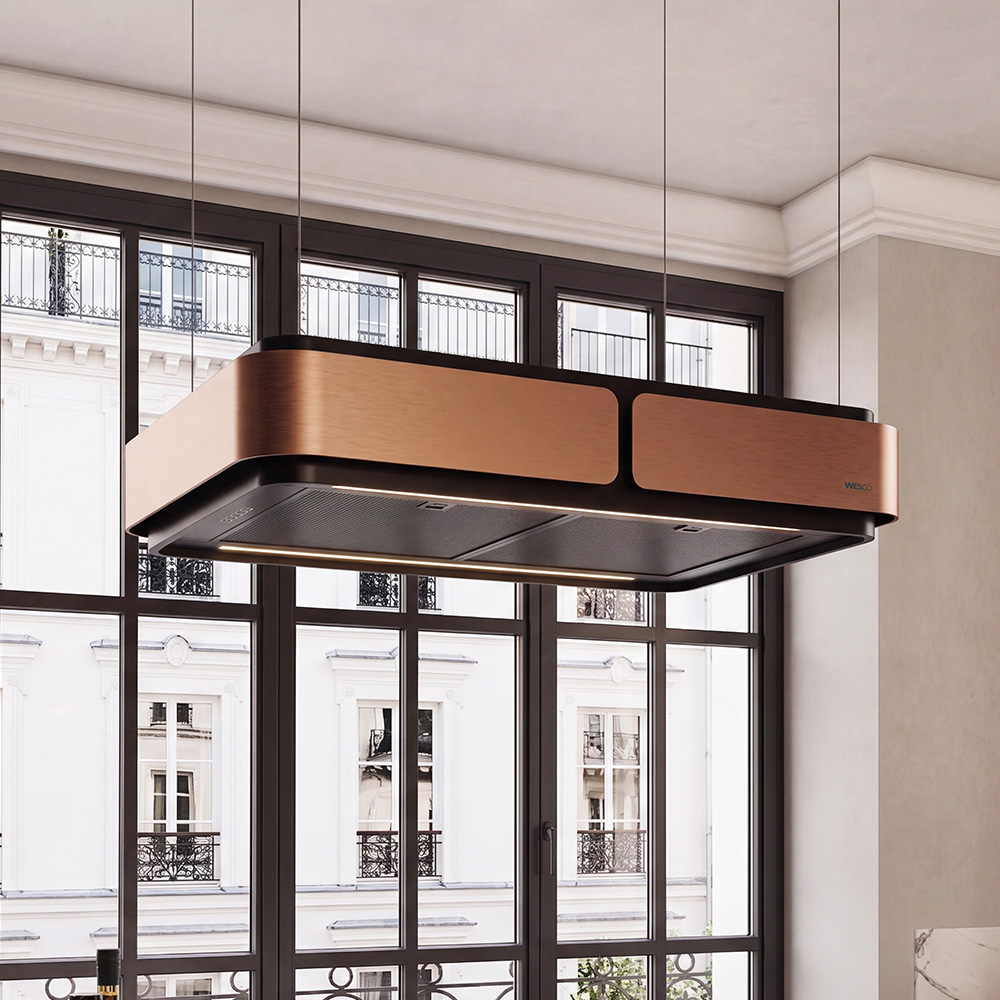 Hotte îlot WESCO Aurea en noir mat avec accents cuivrés et éclairage LED intégré au-dessus d’un îlot de cuisine dans une cuisine ouverte moderne.