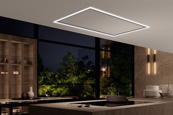 Hotte plafonnier WESCO Volano avec bandeau lumineux LED périphérique allumé au-dessus d’un îlot de cuisine moderne.
