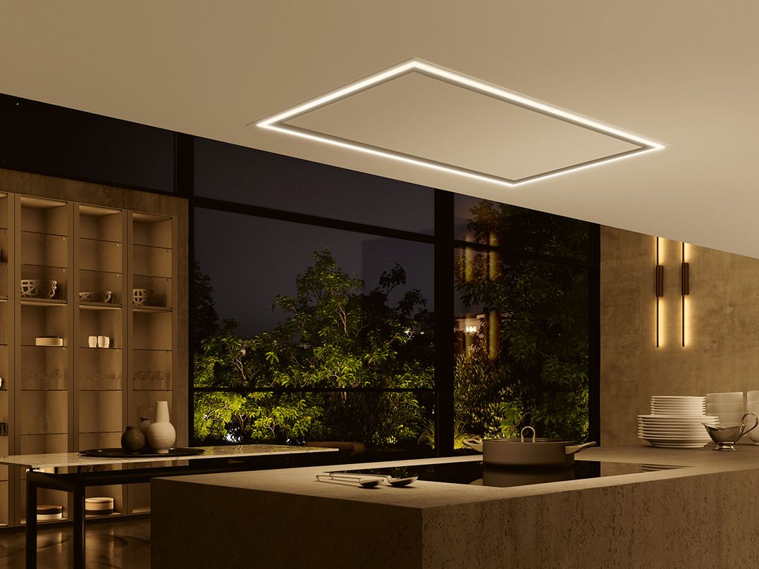 Hotte plafonnier WESCO Volano avec bandeau lumineux LED périphérique allumé au-dessus d’un îlot de cuisine moderne.